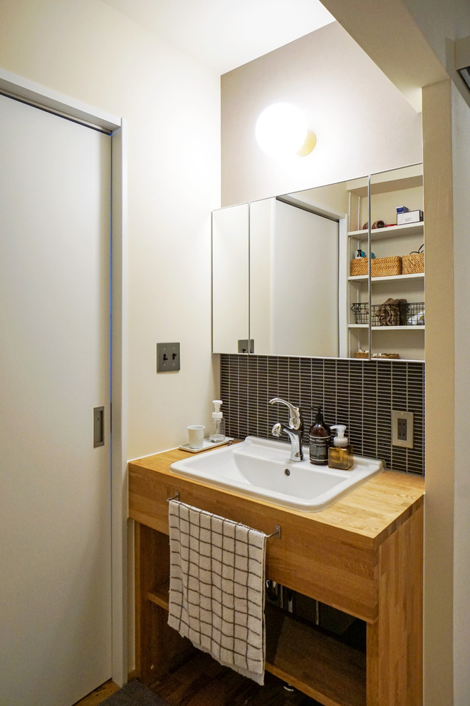 Idée de décoration pour un WC et toilettes asiatique en bois brun avec un placard sans porte, un carrelage noir, mosaïque, un mur beige, un lavabo posé, un plan de toilette en bois et un plan de toilette marron.