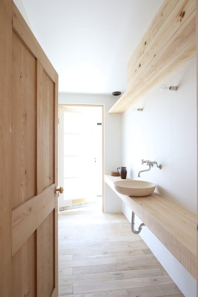 Modelo de aseo rural con paredes blancas, suelo de madera clara, lavabo sobreencimera, encimera de piedra caliza, suelo beige y encimeras beige