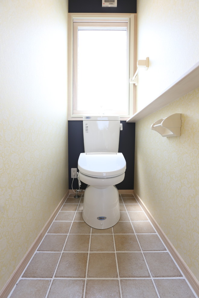 Inredning av ett minimalistiskt toalett, med en toalettstol med hel cisternkåpa, beige kakel, porslinskakel, gula väggar, klinkergolv i porslin, ett piedestal handfat och träbänkskiva