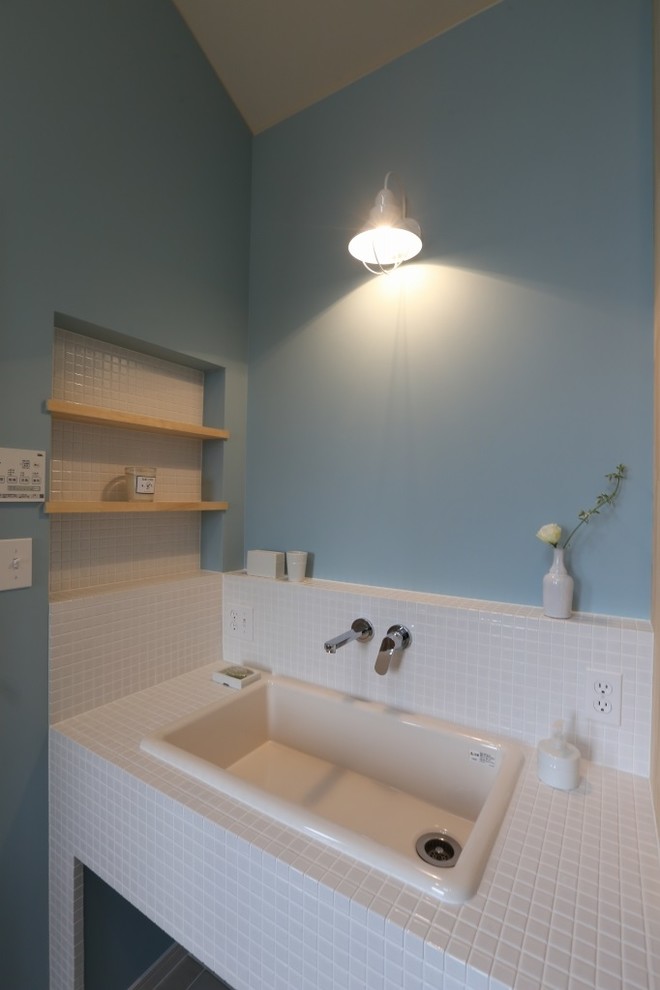 Shabby-Style Gästetoilette mit offenen Schränken, hellen Holzschränken, weißen Fliesen, Mosaikfliesen, blauer Wandfarbe, Einbauwaschbecken und gefliestem Waschtisch in Sonstige