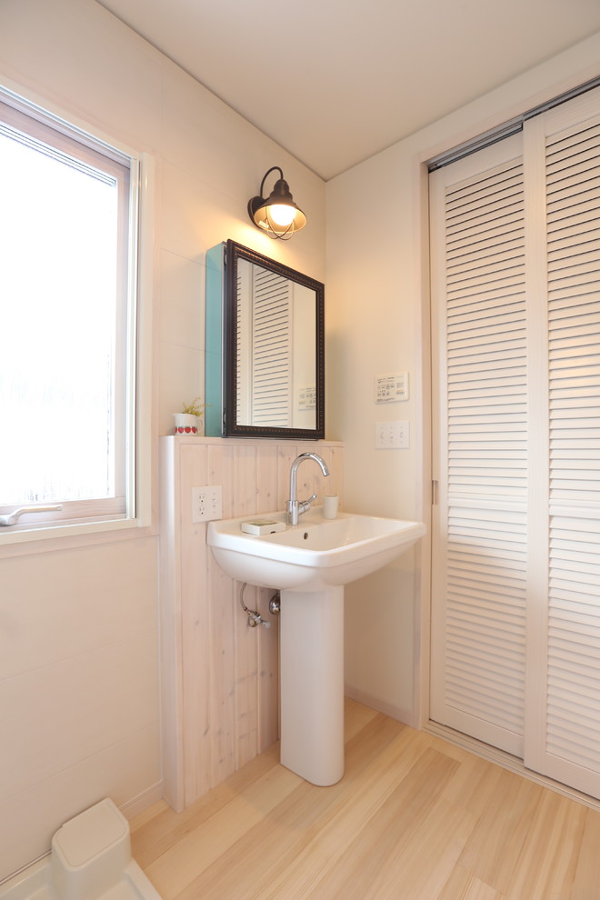 Inredning av ett minimalistiskt toalett, med luckor med lamellpanel, vita skåp, vita väggar, ljust trägolv, ett piedestal handfat och träbänkskiva