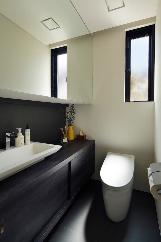 Exemple d'un WC et toilettes tendance avec des portes de placard noires, un bidet, un carrelage blanc, un mur blanc, un sol en carrelage de porcelaine, un lavabo posé, un plan de toilette en bois, un sol gris, un plan de toilette noir, meuble-lavabo encastré et du papier peint.