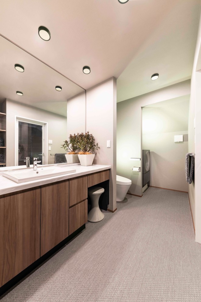 Medium sized modern cloakroom in Tokyo with freestanding cabinets, brown cabinets, a one-piece toilet, grey walls, laminate floors, a built-in sink, solid surface worktops, grey floors and white worktops.