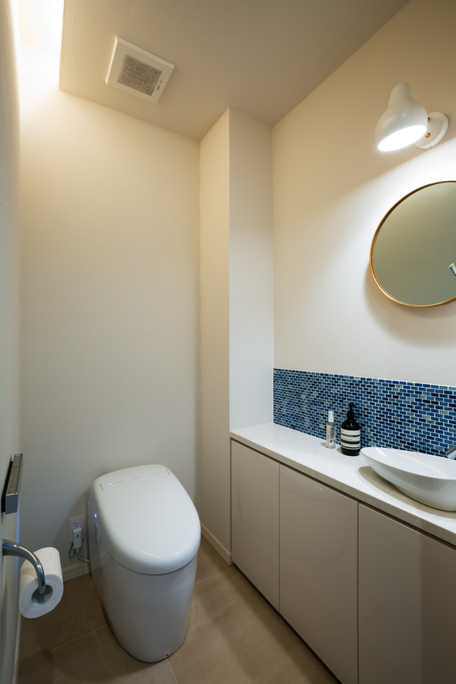 東京23区にある小さな北欧スタイルのおしゃれなトイレ・洗面所 (白いキャビネット、モザイクタイル、ベージュの壁、セラミックタイルの床、オーバーカウンターシンク、グレーの床、白い洗面カウンター、フラットパネル扉のキャビネット、青いタイル、木製洗面台) の写真