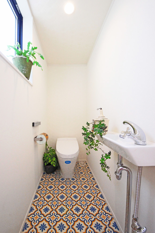 На фото: туалет в восточном стиле с белыми стенами, консольной раковиной и разноцветным полом с