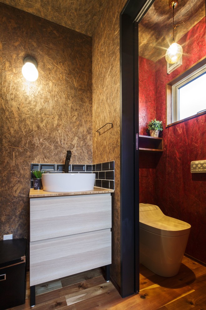 Пример оригинального дизайна: туалет в стиле лофт с плоскими фасадами, светлыми деревянными фасадами, черной плиткой, коричневыми стенами, паркетным полом среднего тона, настольной раковиной и коричневым полом