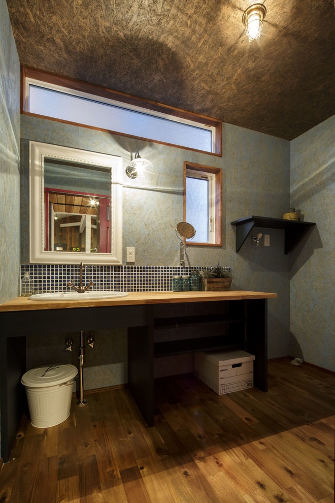 Bild på ett industriellt brun brunt toalett, med öppna hyllor, blå väggar, mellanmörkt trägolv, ett nedsänkt handfat, träbänkskiva och brunt golv