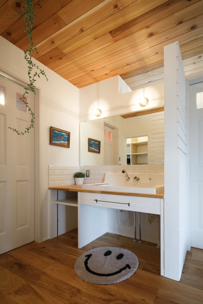Cette image montre un WC et toilettes marin avec un placard à porte plane, des portes de placard blanches, un carrelage blanc, un mur blanc, un sol en bois brun, une vasque, un plan de toilette en bois, un sol marron et un plan de toilette blanc.