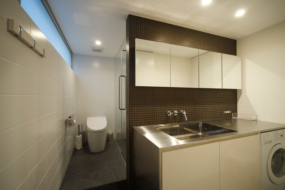 Идея дизайна: туалет в современном стиле с плоскими фасадами, белыми фасадами, унитазом-моноблоком, коричневой плиткой, белыми стенами, монолитной раковиной и столешницей из нержавеющей стали