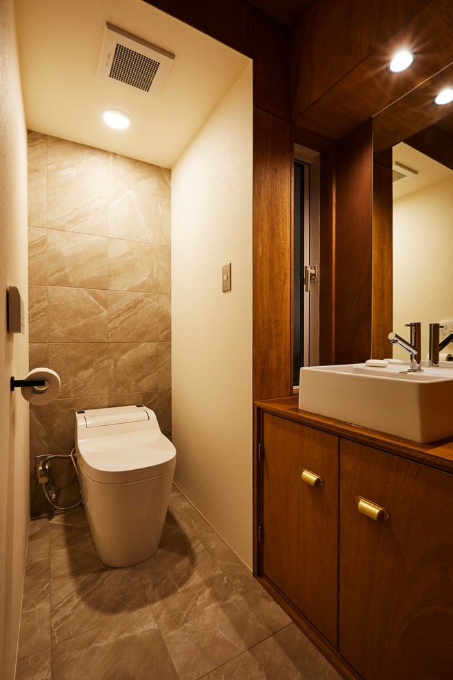 Foto på ett mellanstort funkis brun toalett, med släta luckor, skåp i mörkt trä, en bidé, grå kakel, porslinskakel, bruna väggar, klinkergolv i porslin, ett fristående handfat, träbänkskiva och grått golv