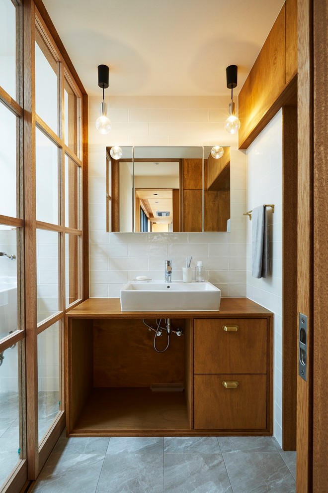 На фото: туалет среднего размера в стиле модернизм с плоскими фасадами, темными деревянными фасадами, белой плиткой, керамогранитной плиткой, белыми стенами, полом из керамогранита, настольной раковиной, столешницей из дерева, серым полом и коричневой столешницей