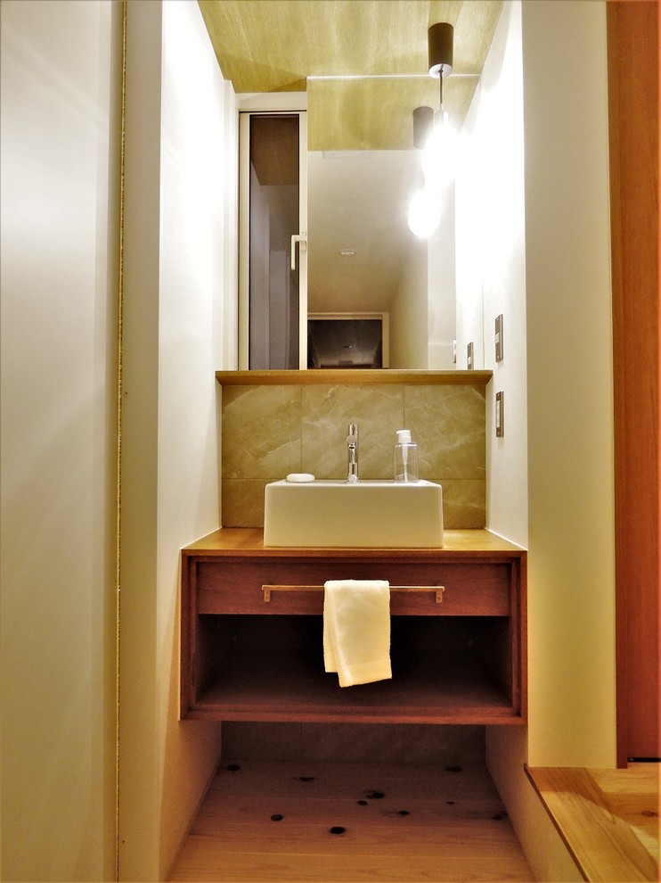 На фото: туалет среднего размера в стиле модернизм с плоскими фасадами, темными деревянными фасадами, биде, серой плиткой, керамогранитной плиткой, белыми стенами, светлым паркетным полом, настольной раковиной, столешницей из дерева, коричневым полом и коричневой столешницей