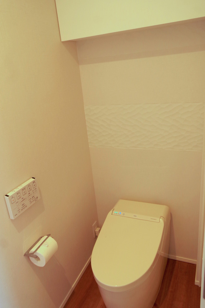 Idéer för att renovera ett funkis toalett, med släta luckor, vita skåp, en toalettstol med hel cisternkåpa, vita väggar, plywoodgolv och brunt golv