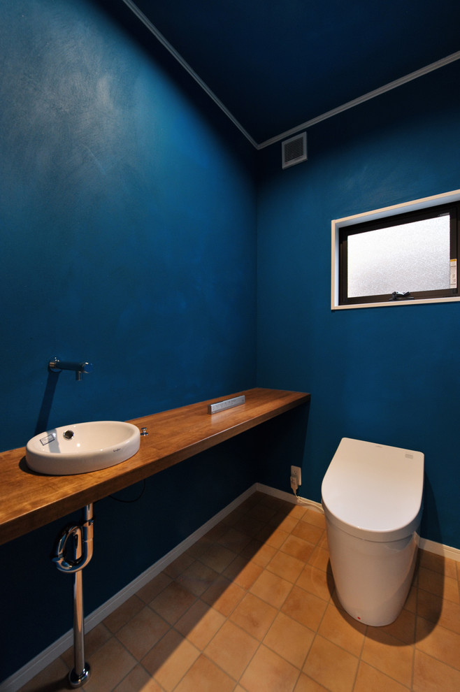 他の地域にあるエクレクティックスタイルのおしゃれなトイレ・洗面所 (青い壁、テラコッタタイルの床、オーバーカウンターシンク、木製洗面台、青い床、ブラウンの洗面カウンター) の写真