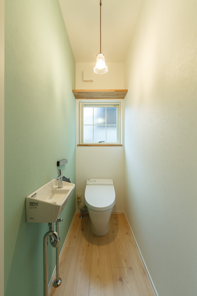 Inspiration for a contemporary cloakroom in Other with a one-piece toilet, multi-coloured walls, light hardwood flooring, a wall-mounted sink and beige floors.