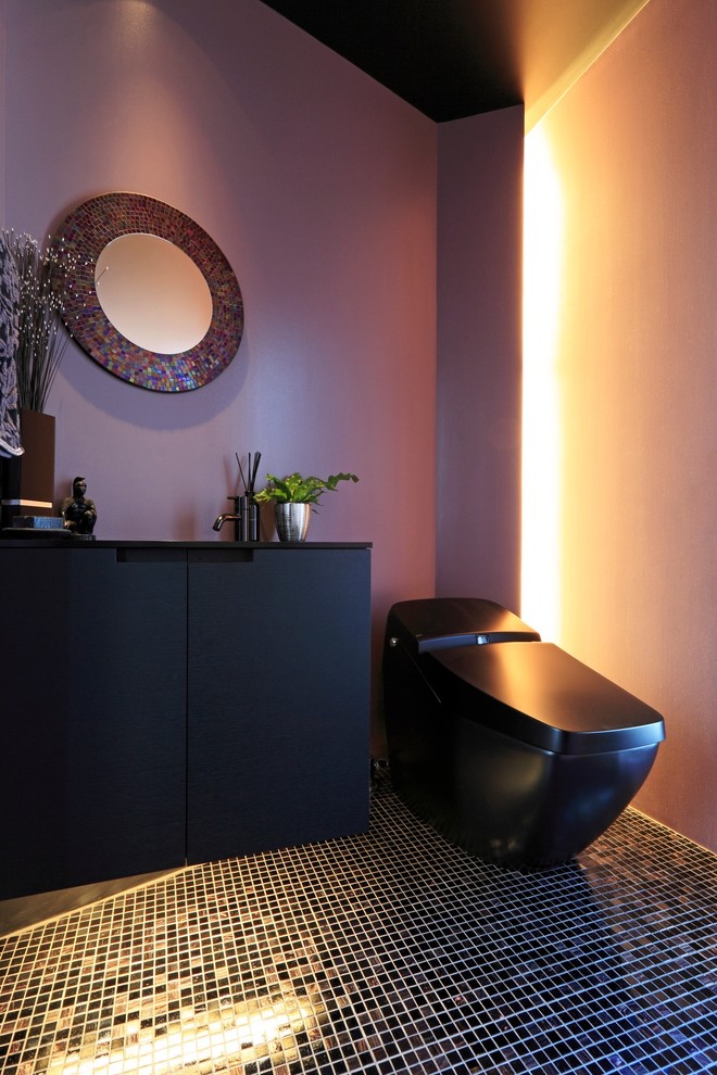 Cette image montre un WC et toilettes design avec un placard à porte plane, des portes de placard noires, un mur violet, un lavabo posé et un sol noir.