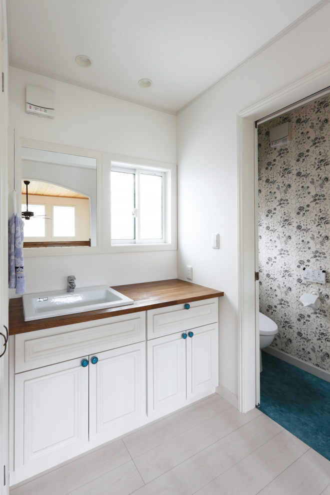 他の地域にある北欧スタイルのおしゃれなトイレ・洗面所 (落し込みパネル扉のキャビネット、白いキャビネット、白い壁、オーバーカウンターシンク、木製洗面台、マルチカラーの床) の写真
