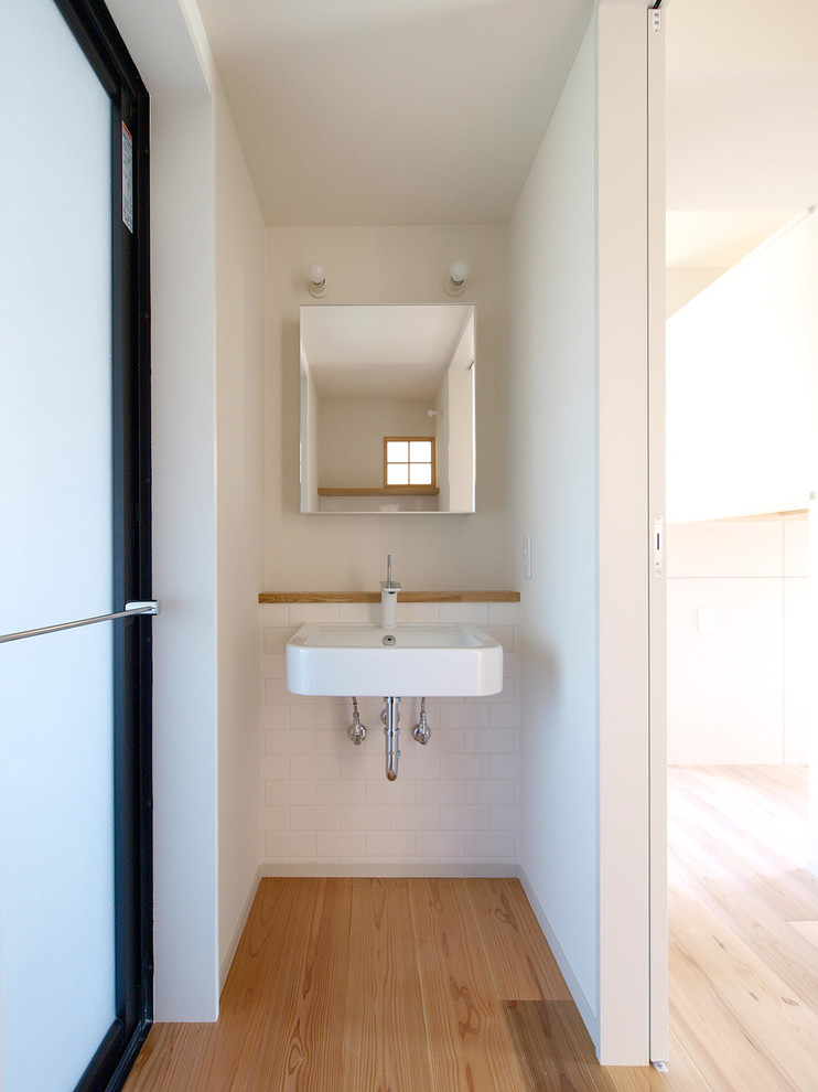 Inspiration för 60 tals toaletter, med vit kakel, porslinskakel, ljust trägolv och ett väggmonterat handfat