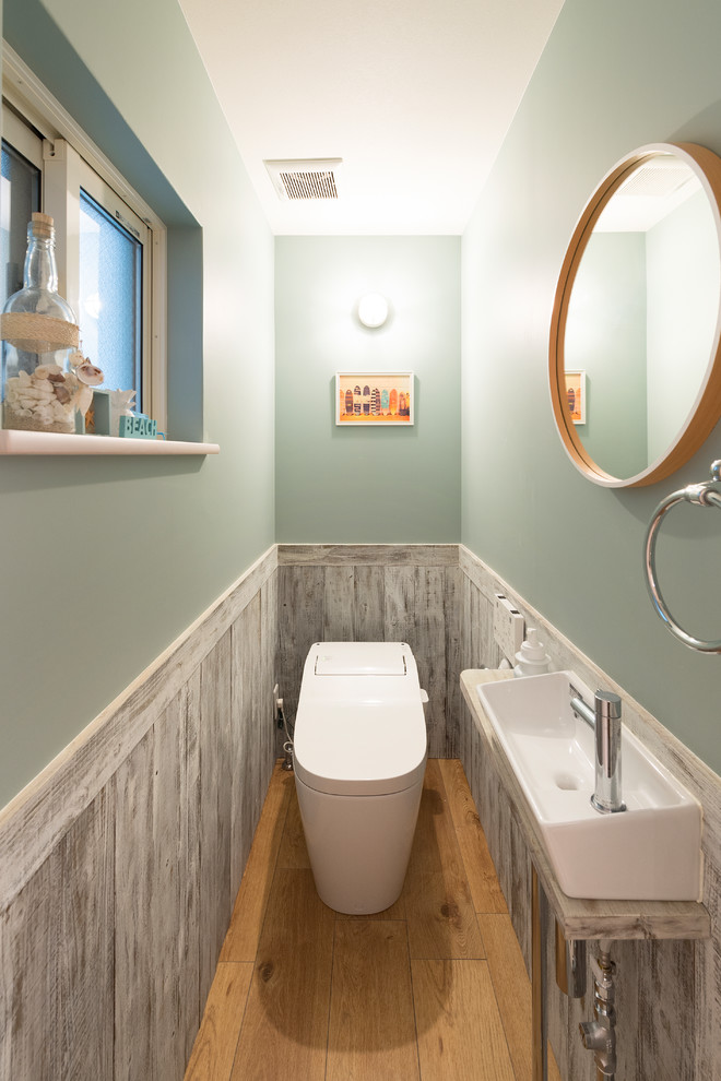Cette image montre un petit WC et toilettes marin avec un mur bleu, un sol en bois brun, une vasque et un sol beige.