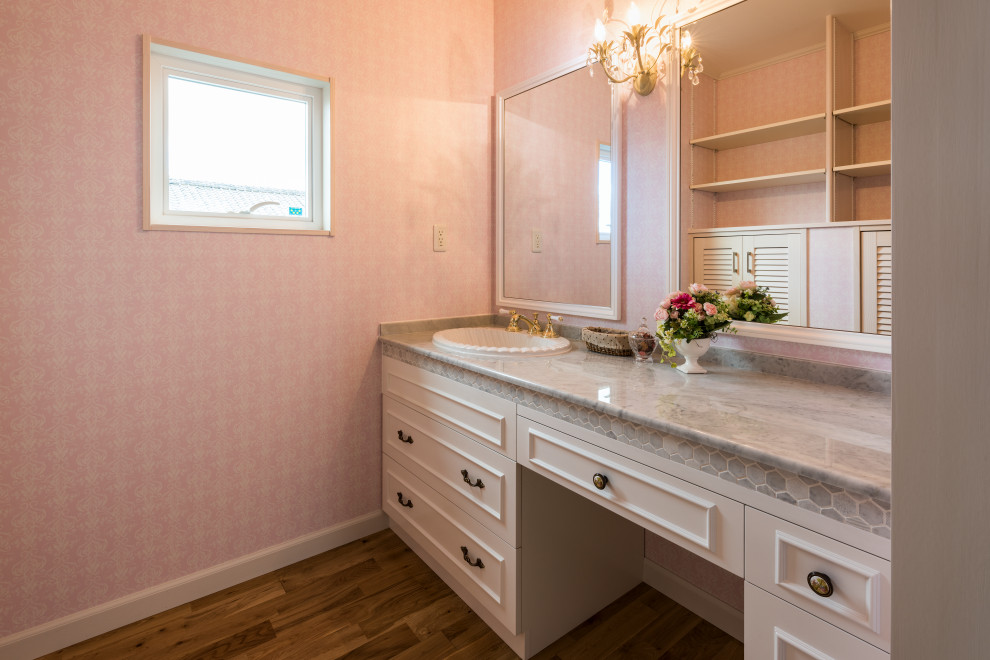 Idéer för att renovera ett stort minimalistiskt vit vitt toalett, med möbel-liknande, bruna skåp, en toalettstol med hel cisternkåpa, rosa kakel, keramikplattor, rosa väggar, mellanmörkt trägolv, ett integrerad handfat, marmorbänkskiva och brunt golv