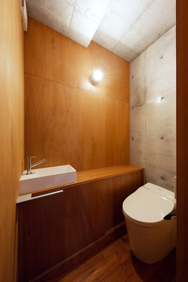 Foto på ett industriellt brun toalett, med släta luckor, skåp i mellenmörkt trä, flerfärgade väggar, mellanmörkt trägolv, ett fristående handfat, träbänkskiva och brunt golv