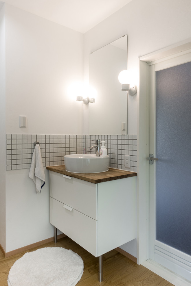 Пример оригинального дизайна: туалет среднего размера в скандинавском стиле с плоскими фасадами, белыми фасадами, белыми стенами, деревянным полом, настольной раковиной и коричневым полом