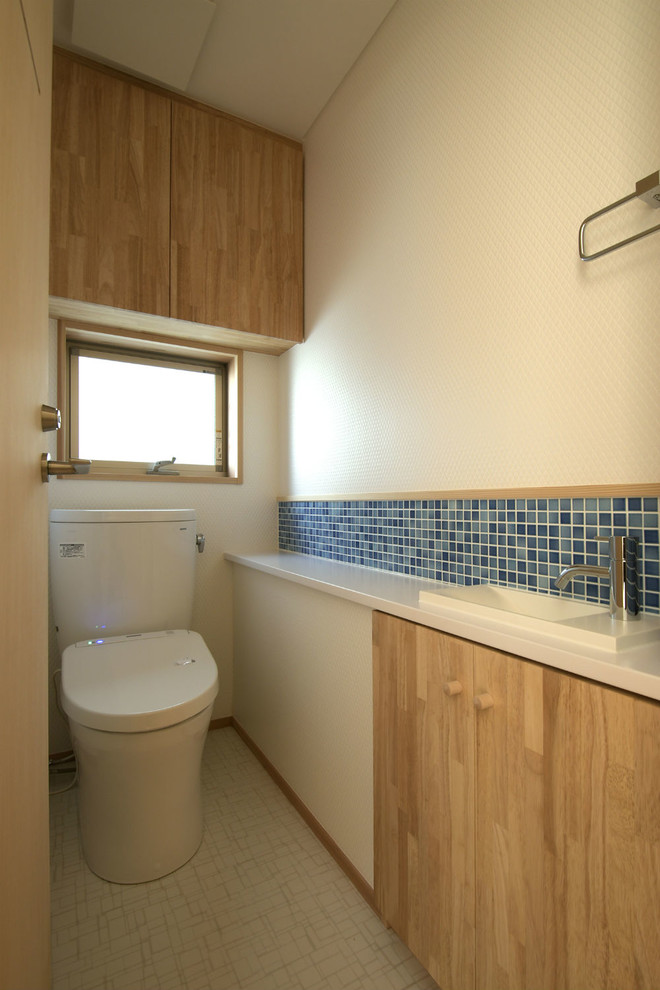 Foto på ett stort amerikanskt toalett, med släta luckor, skåp i mellenmörkt trä, en toalettstol med hel cisternkåpa, blå kakel, mosaik, vita väggar, vinylgolv, ett nedsänkt handfat, bänkskiva i akrylsten och vitt golv