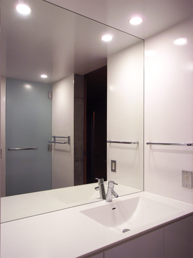 Cette photo montre un WC et toilettes moderne en bois foncé avec un placard à porte plane, un mur blanc, un lavabo intégré et un plan de toilette en surface solide.