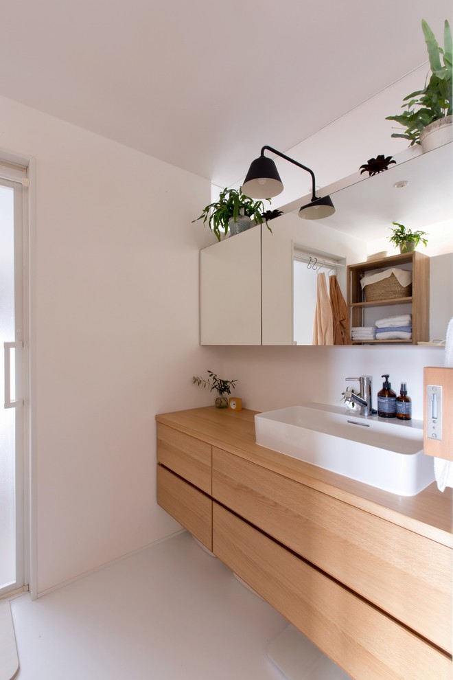 This is an example of a medium sized world-inspired cloakroom in Other with flat-panel cabinets, brown cabinets, white walls, a vessel sink, brown worktops, a two-piece toilet, white tiles, porcelain tiles, medium hardwood flooring, solid surface worktops and beige floors.