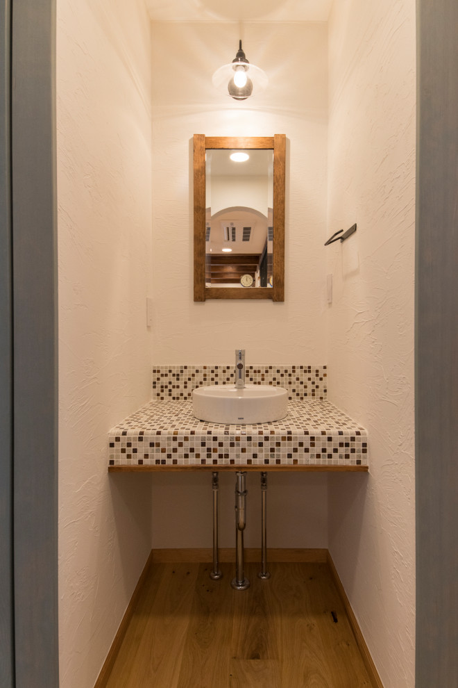 Exemple d'un WC et toilettes nature en bois foncé avec un placard sans porte, un mur blanc, parquet clair, une vasque, un plan de toilette en carrelage, un sol beige et un plan de toilette multicolore.