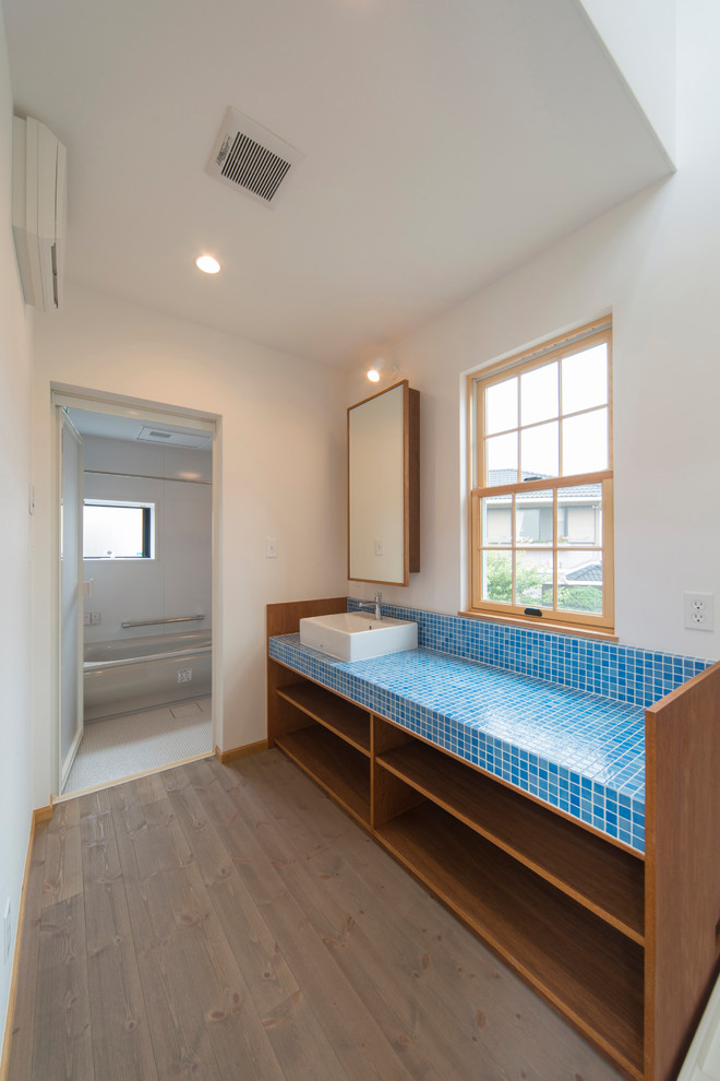 This is an example of a mediterranean cloakroom in Other with open cabinets, dark wood cabinets, orange tiles, white walls, medium hardwood flooring, a vessel sink and tiled worktops.