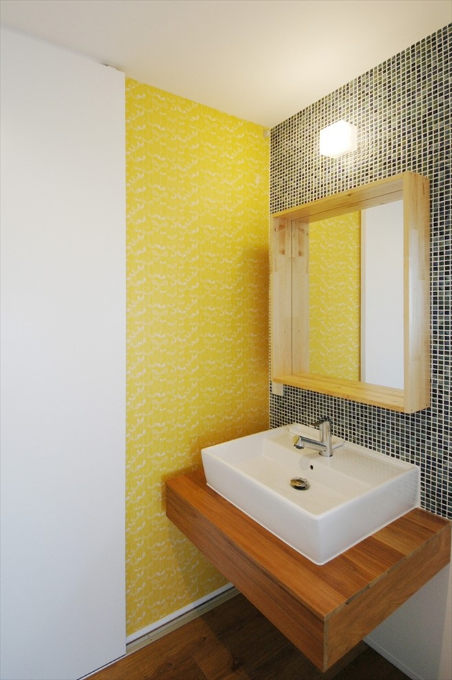 Пример оригинального дизайна: маленький туалет в стиле модернизм с открытыми фасадами, темными деревянными фасадами, синей плиткой, плиткой мозаикой, желтыми стенами, полом из линолеума, подвесной раковиной и столешницей из дерева для на участке и в саду