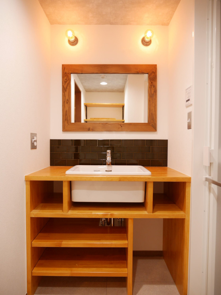Inredning av ett 50 tals litet brun brunt toalett, med vita väggar, vinylgolv, grått golv, öppna hyllor, bruna skåp, grön kakel, porslinskakel, ett undermonterad handfat och träbänkskiva