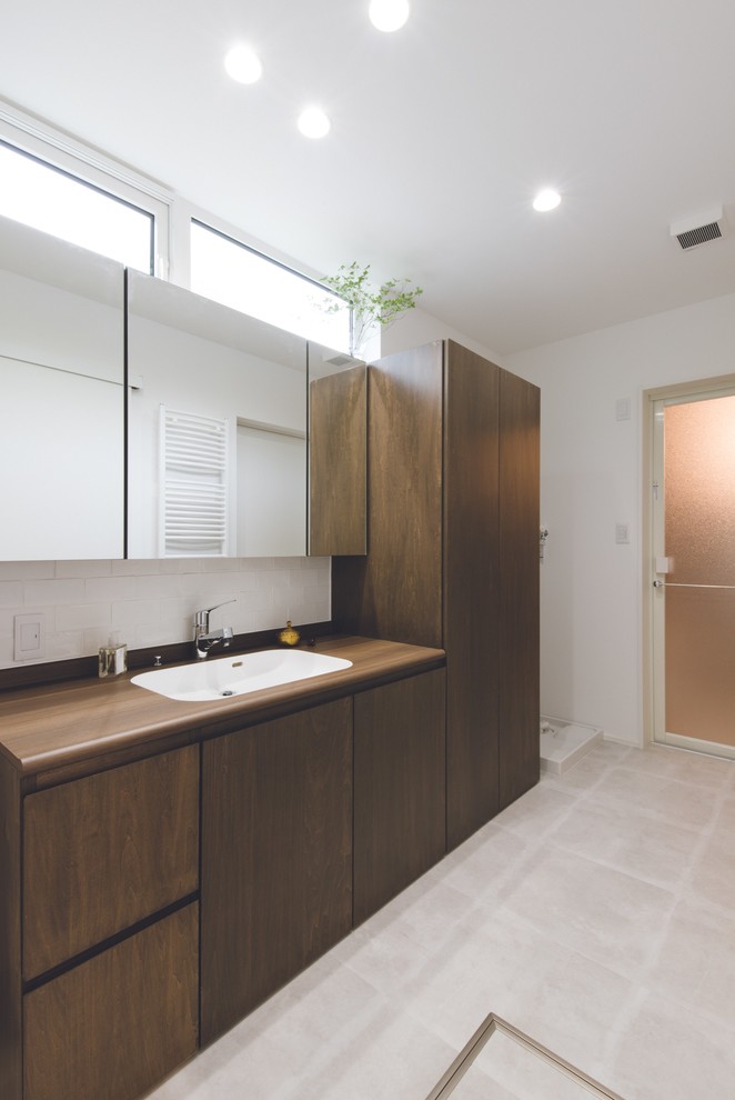 Aménagement d'un grand WC et toilettes scandinave en bois brun avec un placard à porte plane, un mur blanc, un sol en carrelage de céramique, un lavabo encastré et un plan de toilette en bois.
