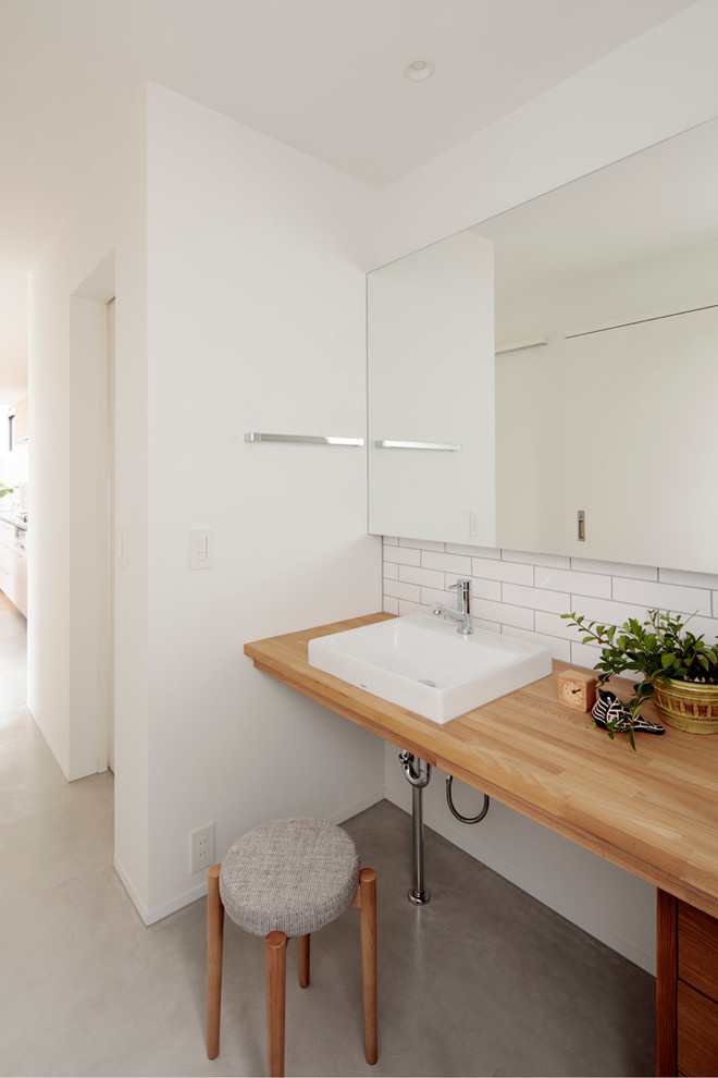 На фото: туалет в скандинавском стиле с белыми стенами, бетонным полом, настольной раковиной, столешницей из дерева, серым полом и коричневой столешницей