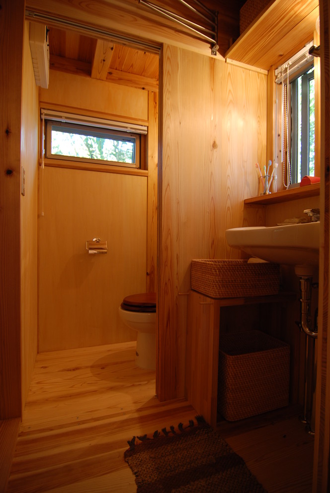 This is an example of a small rustic cloakroom in Other with a one-piece toilet, plywood flooring, a wall-mounted sink, open cabinets and glass tiles.