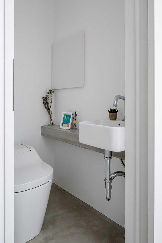 Moderne Gästetoilette mit Toilette mit Aufsatzspülkasten, weißer Wandfarbe, Betonboden, Aufsatzwaschbecken, Beton-Waschbecken/Waschtisch, grauem Boden und grauer Waschtischplatte in Sonstige