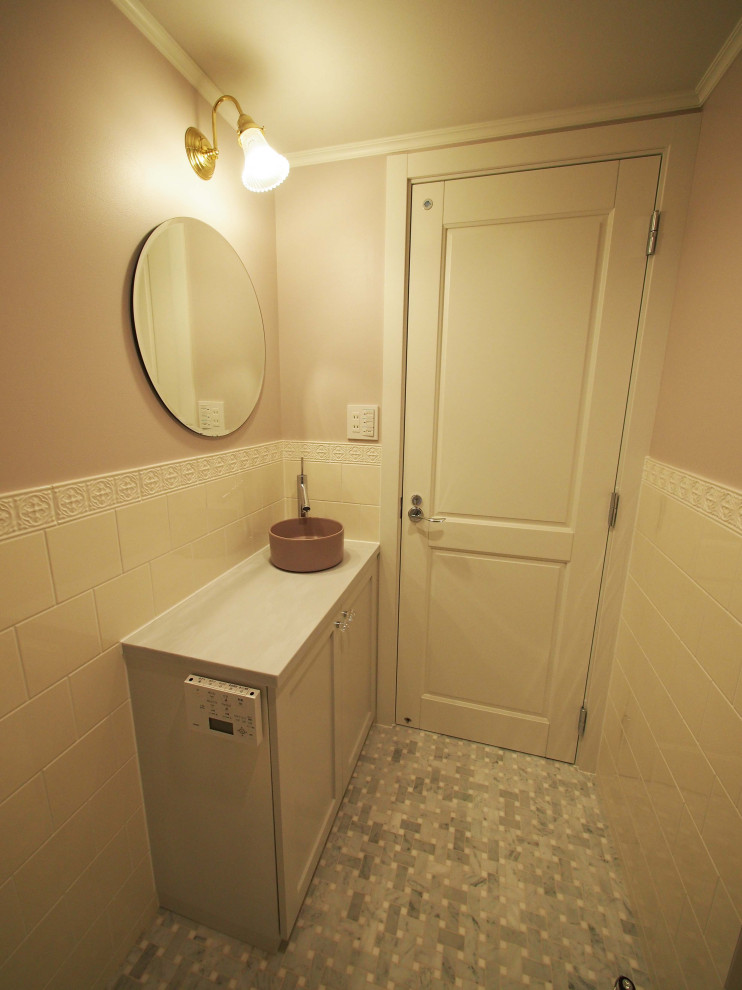 Modern inredning av ett stort vit vitt toalett, med luckor med glaspanel, vita skåp, grå kakel, glaskakel, vita väggar, klinkergolv i keramik, ett undermonterad handfat, bänkskiva i akrylsten och beiget golv