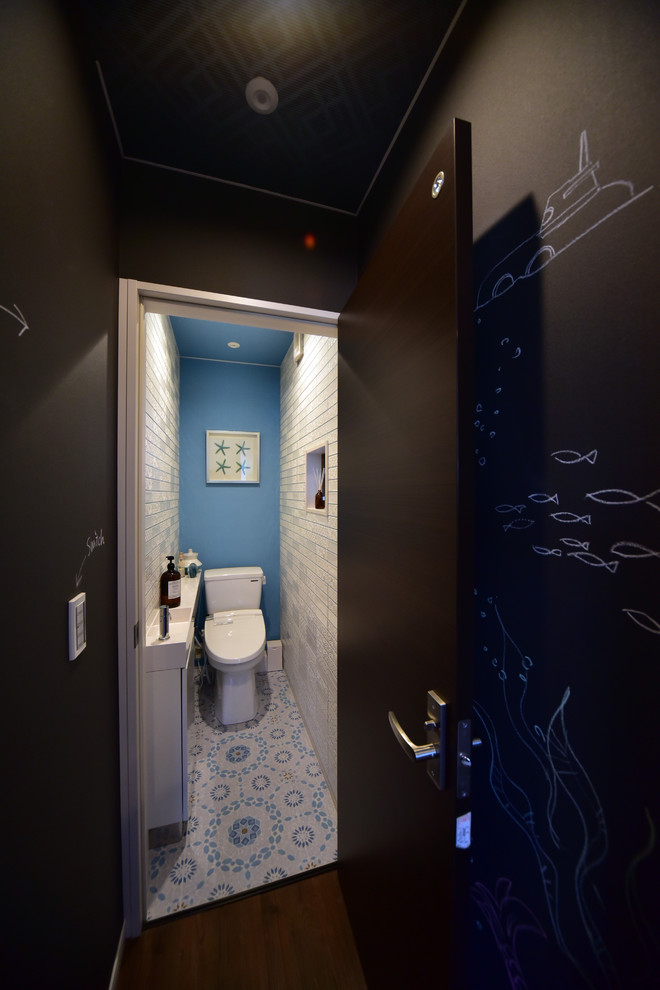 Inspiration pour un petit WC et toilettes marin avec un placard à porte plane, des portes de placard blanches, un sol multicolore, WC à poser, un carrelage blanc, des carreaux de céramique, un mur bleu, un sol en vinyl, un lavabo intégré, un plan de toilette en surface solide et un plan de toilette blanc.