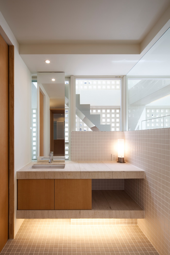 Immagine di un bagno di servizio etnico con ante lisce, ante in legno chiaro, piastrelle beige, pareti bianche, lavabo sottopiano e pavimento grigio