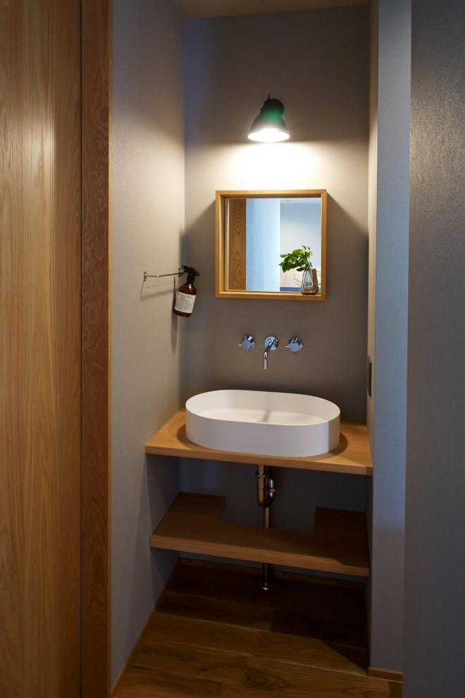 Inspiration pour un WC et toilettes design avec un placard sans porte, un mur gris, un sol en bois brun, une vasque, un plan de toilette en bois, un sol marron et un plan de toilette marron.