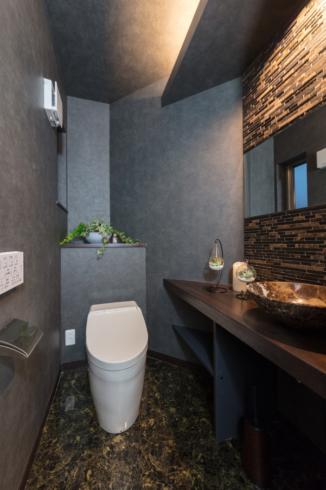 Cette image montre un WC et toilettes minimaliste de taille moyenne avec un placard sans porte, WC à poser, un carrelage marron, mosaïque, un mur gris, un sol en linoléum, un lavabo posé, un plan de toilette en bois, un sol marron et un plan de toilette marron.