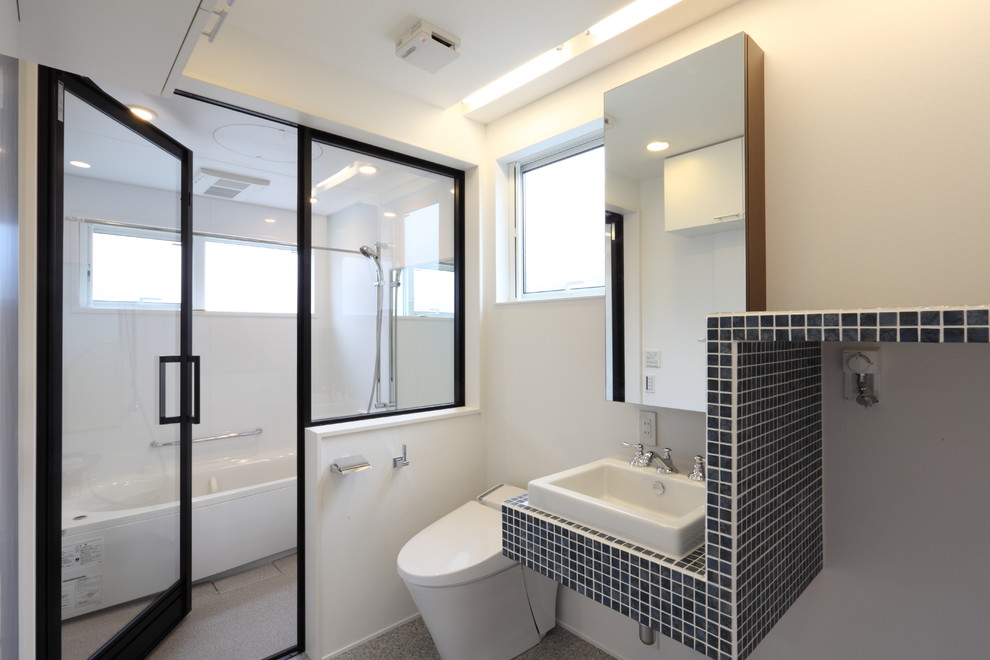 На фото: туалет в современном стиле с белыми стенами, настольной раковиной, серым полом и синей столешницей с