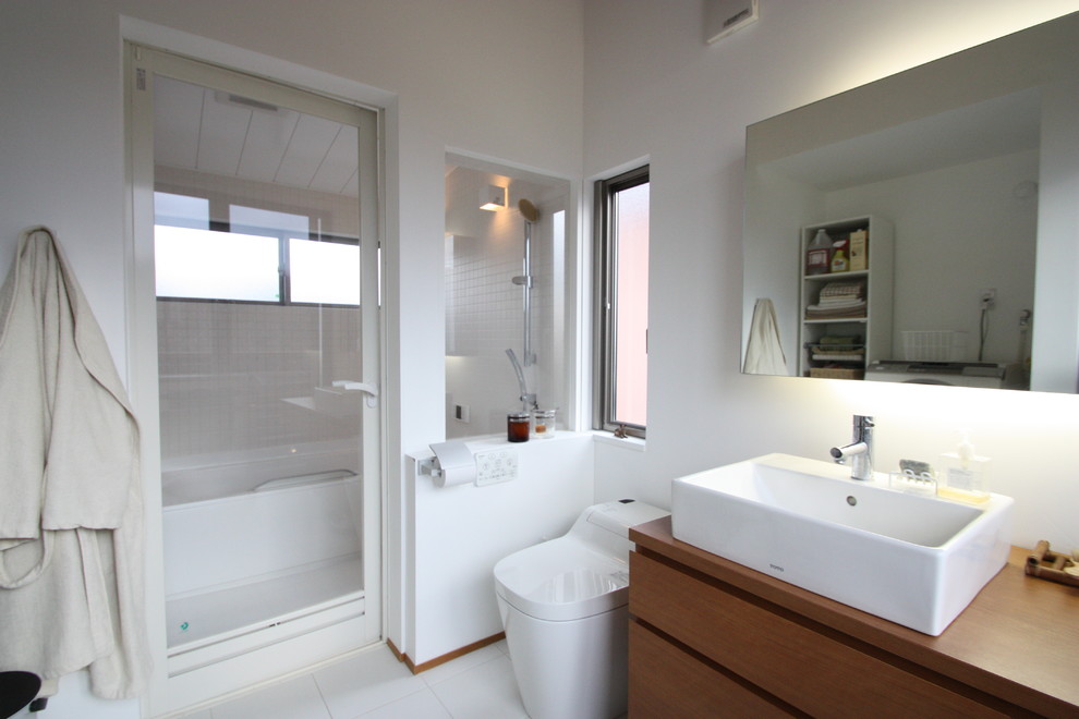 横浜にあるコンテンポラリースタイルのおしゃれなトイレ・洗面所 (白いタイル、白い壁、オーバーカウンターシンク、白い床、ブラウンの洗面カウンター) の写真