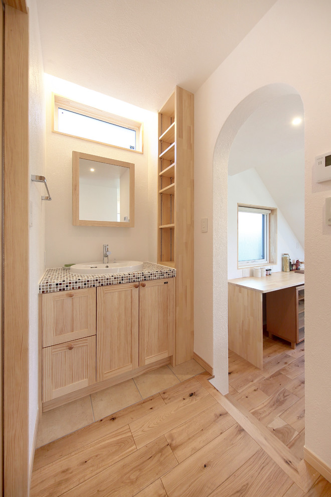 Moderne Gästetoilette mit hellen Holzschränken, weißer Wandfarbe, gefliestem Waschtisch, braunem Boden und brauner Waschtischplatte in Sonstige