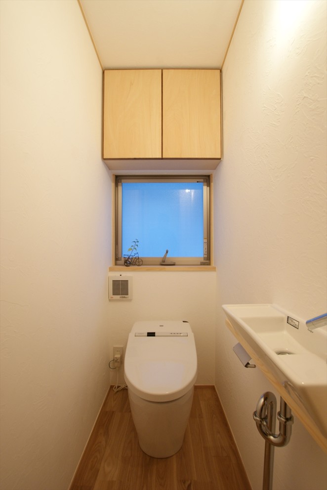 Immagine di un piccolo bagno di servizio moderno con ante lisce, ante in legno chiaro, pareti bianche, pavimento in legno massello medio, lavabo a consolle e pavimento marrone