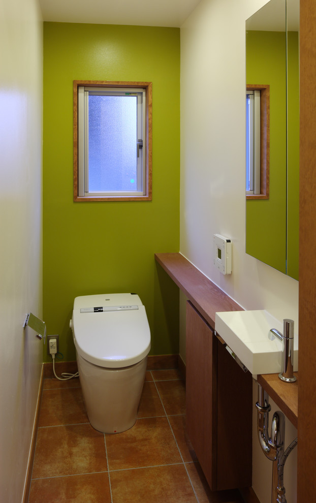 Mid-Century Gästetoilette mit Toilette mit Aufsatzspülkasten, grüner Wandfarbe, Terrakottaboden, Aufsatzwaschbecken, Waschtisch aus Holz und hellbraunen Holzschränken in Tokio Peripherie