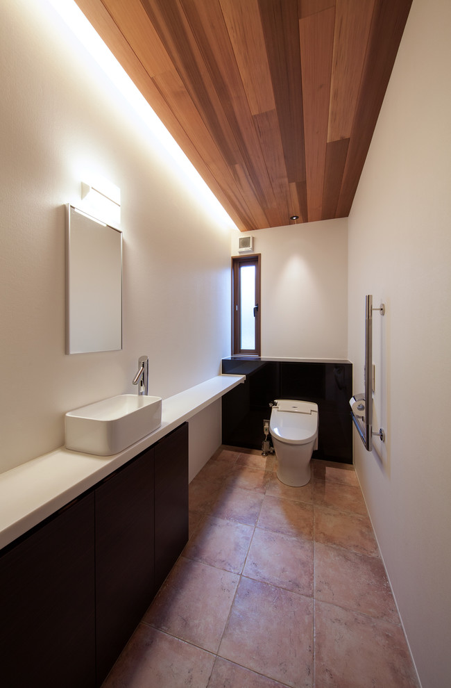 Cette photo montre un WC et toilettes moderne en bois foncé avec un placard à porte plane, un mur blanc, tomettes au sol, une vasque et un sol marron.