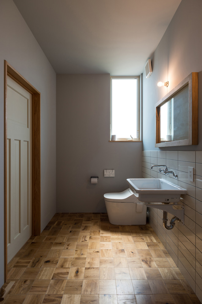 Exemple d'un WC et toilettes industriel avec un carrelage blanc, un mur multicolore, un sol en bois brun, un lavabo suspendu et un sol marron.