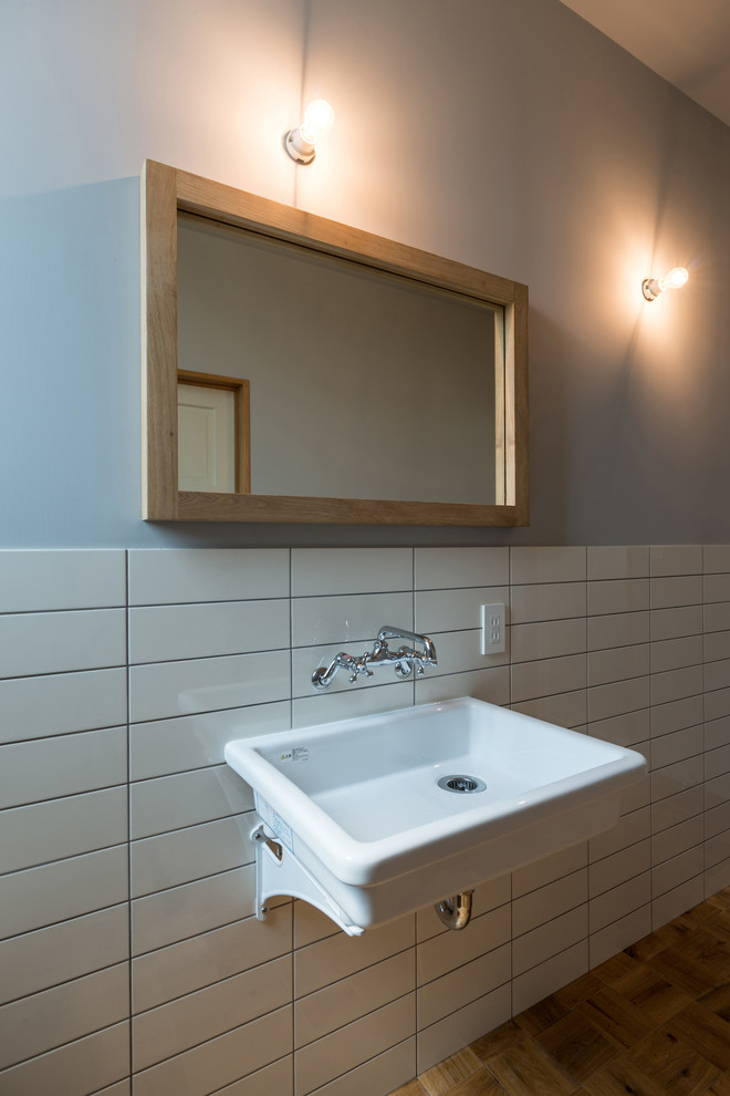 Idee per un bagno di servizio industriale con piastrelle bianche, pareti multicolore, pavimento in legno massello medio, lavabo sospeso e pavimento marrone